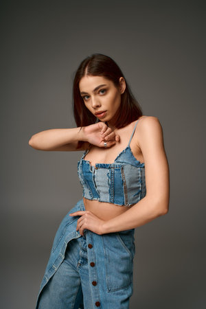 A stylish young woman in a denim outfit confidently poses in a modern studio space, radiating bliss.の写真素材
