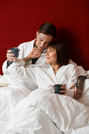 In a stylish hotel room, a young couple cuddles together, sharing a warm drink and love.の写真素材