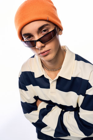 Teenager poses confidently in a striped long sleeve polo and orange hat against a white backdrop.の写真素材