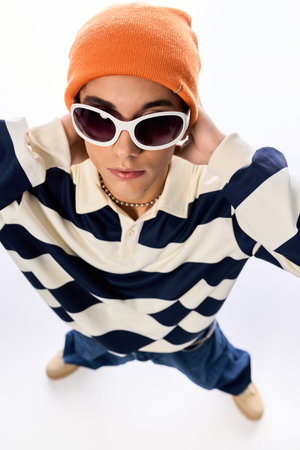 Teen in a striped polo and orange hat poses confidently against a bright backdrop.の写真素材