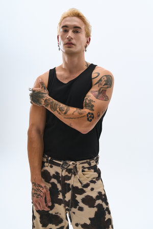Handsome young man confidently poses in trendy attire with striking tattoos on display.の写真素材