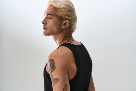 Young man showcases modern fashion with a confident pose, highlighting his tattoos and hairstyle.の写真素材