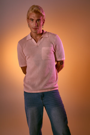 A young man stylishly poses in a modern outfit, lit by warm light that showcases his fashion.の写真素材