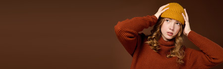 A pretty redhead poses in a warm winter sweater and hat against a rich brown backdrop, bannerの写真素材