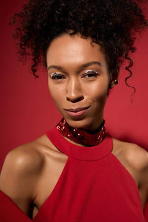 A young woman elegantly poses, showcasing her charm and style in a vibrant red backdrop.