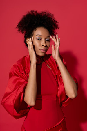 A young woman expresses joy and confidence, gently touching her face while dressed in striking red.の写真素材