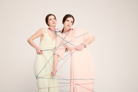 Twin sisters in a studio playfully interact with vibrant strings while showcasing elegant fashion.の写真素材