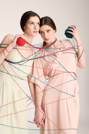 Young beautiful twin sisters express their fashion sense using vibrant yarn in a studio space.の写真素材