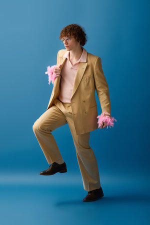 A trendy teen poses in a light suit with playful accents against a blue background.の写真素材