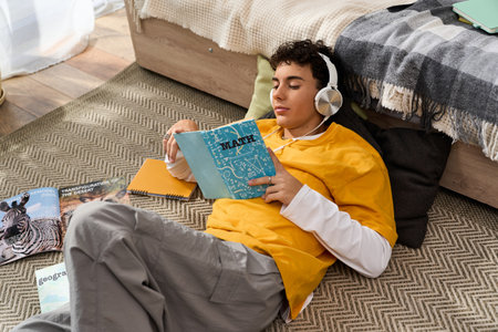 Stylish teenager enjoys reading a math book on the floor, surrounded by study materials and comfort.の写真素材