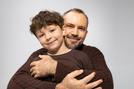 A smiling father hugs his cheerful little son, radiating love and happiness in a cozy setting.の写真素材