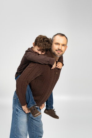 A father enjoys a playful moment, giving his son a piggyback ride with smiles all around.の写真素材