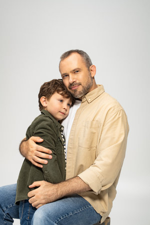 A man gently holds his little son, both smiling and enjoying a tender moment together at home.の写真素材