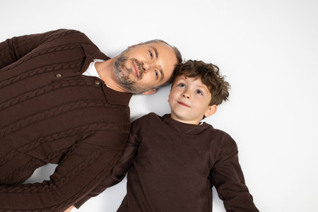 A father and his little son share a delightful moment while lying side by side, smiling happily.の写真素材