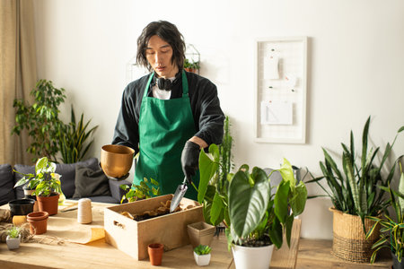 A young asian florist carefully tends to vibrant plants while arranging them in a cozy indoor space.