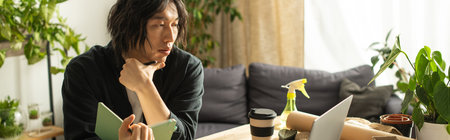 A young Asian man, focused and thoughtful, designs floral arrangements surrounded by greenery.の写真素材