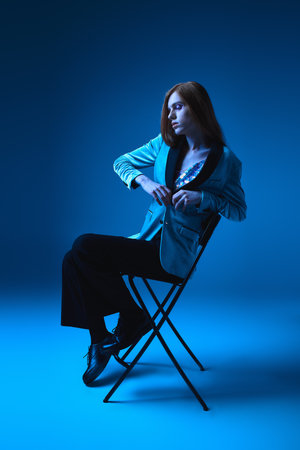 A stylishly dressed person exudes confidence, seated against a blue backdrop.の写真素材