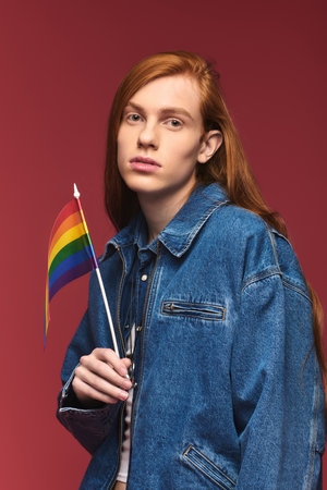 A young person stands confidently, holding a rainbow flag, showcasing pride and unity.