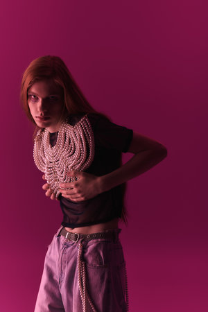 A person showcases unique style with a pearl necklace against a bright pink backdrop.の写真素材