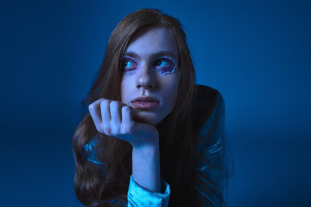 A person showcases unique makeup and styling in a soft blue light, reflecting their pride.の写真素材