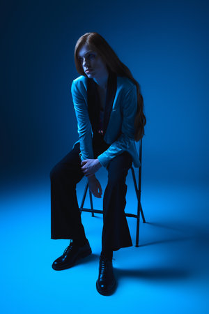 A lgbt individual seated on a chair, reflecting confidence and beauty in a blue lit environment.の写真素材