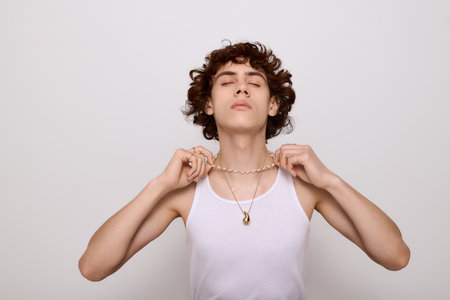 Confident young man in a tank top adjusts his necklace, showcasing style and poise.の写真素材