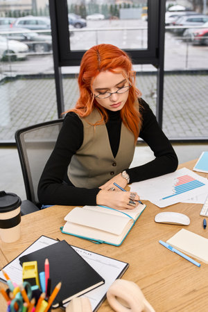 Bright workspace filled with tools as a young woman writes notes with focus and creativity.の写真素材