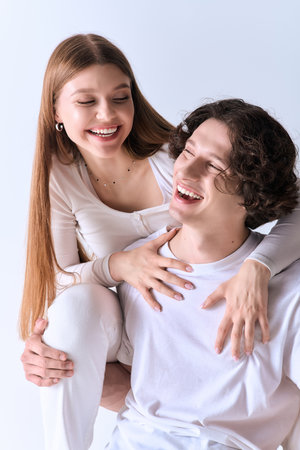 A joyful couple smiles together in a grey studio, enjoying each other's company.