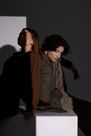 Young couple poses in chic outfits, embracing each other's style in a dark grey studio.