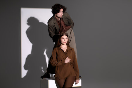 A stylish young couple poses creatively in a dark studio, showcasing their outfits.