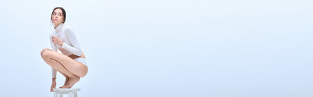 A stylish woman exudes elegance while squatting on a stool in a simple setting.の写真素材