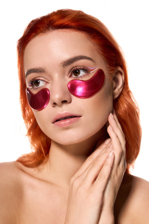 Beautiful woman with striking orange hair applies chic eye masks, radiating confidence and style.の写真素材
