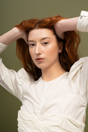 A young woman with red hair models her chic spring outfit gracefully in a studio.の写真素材