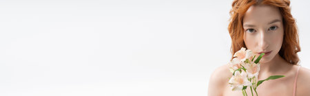 A young redhead poses gracefully with flowers, showcasing spring beauty in a studio, bannerの写真素材