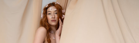 A young woman with red hair poses elegantly among blooming flowers in a beige setting, bannerの写真素材