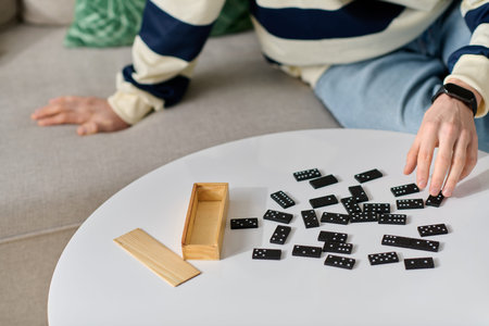 A young man with a charming smile plays dominoes on a stylish coffee table at home.