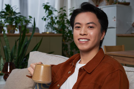 An asian man enjoys a relaxing moment at home, sipping from a warm mug in his stylish apartment.