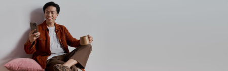 A man relaxes in his chic apartment, smiling at his smartphone with a coffee in hand, banner