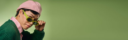 An asian man models a trendy outfit and sunglasses in a green studio, blending style with personality, bannerの写真素材