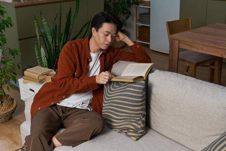 An Asian man enjoys a quiet afternoon reading in his stylish home, surrounded by plants.の写真素材