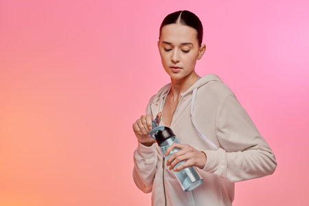 In a cozy setting, a fashionable young woman opens a water bottle, embracing hydration with grace.