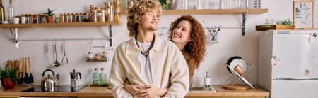 A curly-haired couple blissfully embraces in their stylish kitchen, radiating warmth and joy, banner