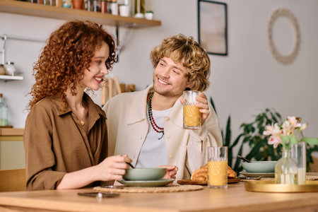 Two curly-haired young people share a cheerful breakfast in their stylish home, savoring the moment.