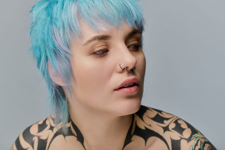 A young woman shows off her blue hair and artistic tattoos against a neutral background.