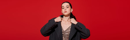 A beautiful woman showcases her stylish outfit with grace, set against a vibrant red background.の写真素材