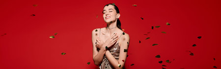 Joyful woman embraces the moment, surrounded by falling golden accents in a striking red setting.の写真素材