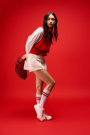 A young cheerleader confidently shows off her sporty style with pom poms in a bold red setting.