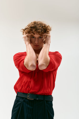 A stylish young man with curly hair poses in a vibrant red shirt in a modern studio.