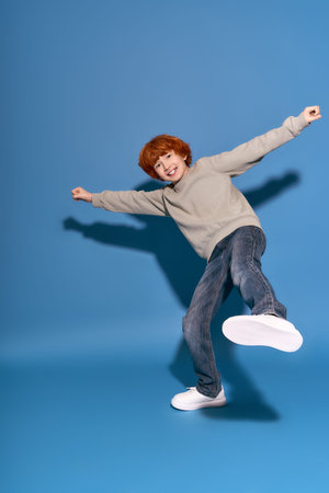 A cheerful little boy with curly red hair is dancing playfully in a stylish outfit.