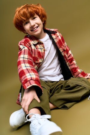 Brightly dressed boy with orange hair sits happily on a soft backdrop, showcasing his playful style.の写真素材